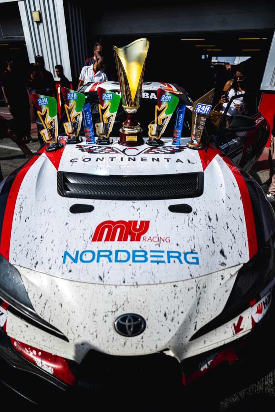 The gold winner's trophy and four class cups standing on the bonnet of the Continental Toyota Supra GT4, the car still dirty from the race