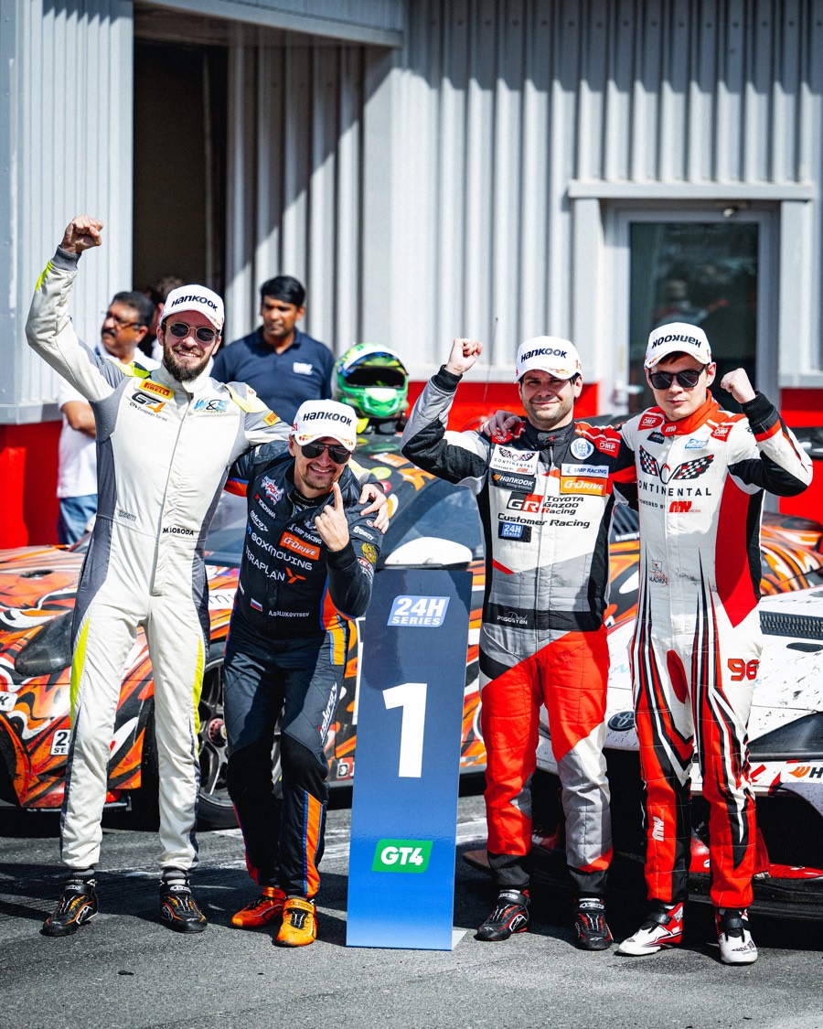 Four drivers throw their fists up behind the number one board after a GT4 class win