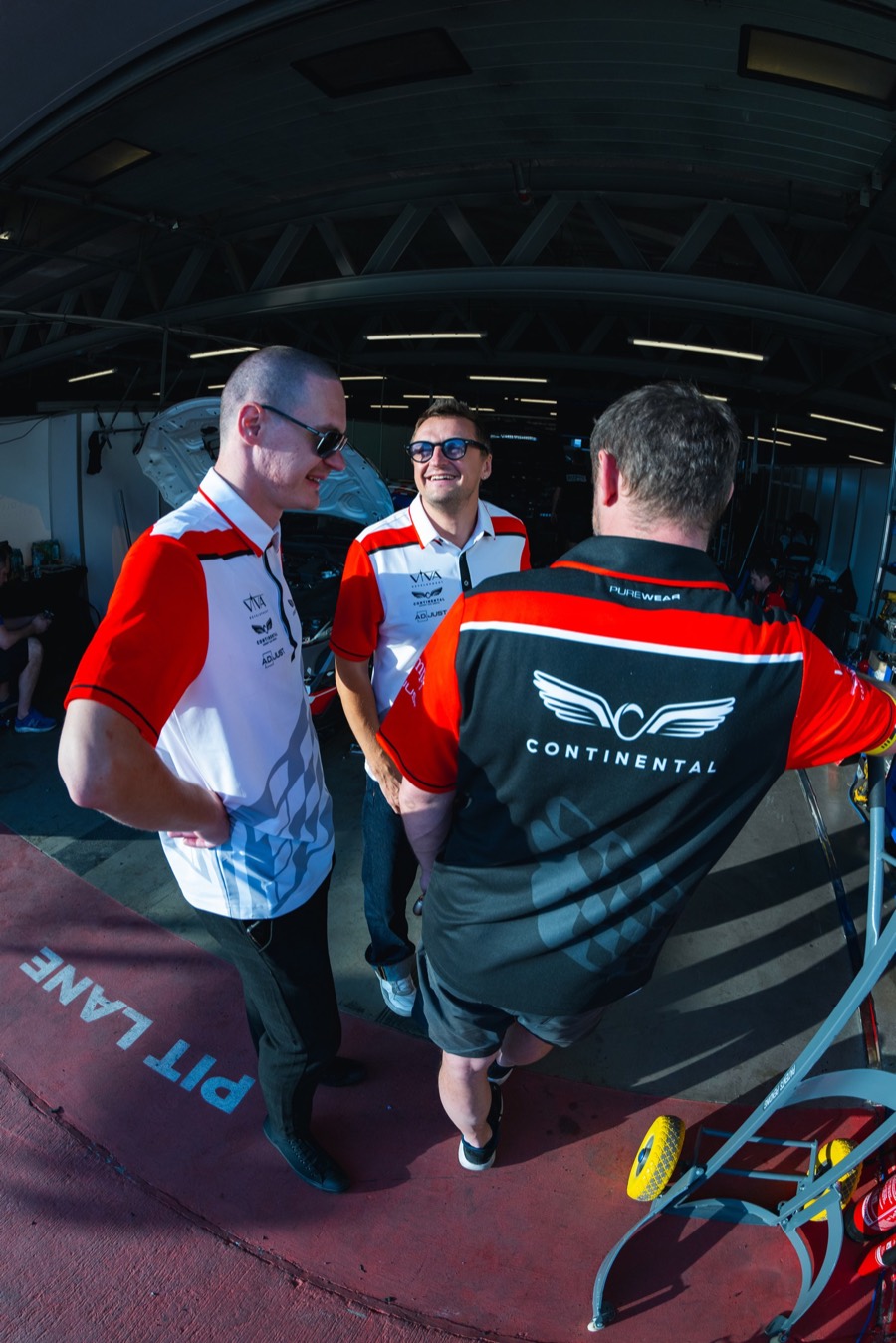 Three of the team talking in the pit lane, the lane's own markings underfoot