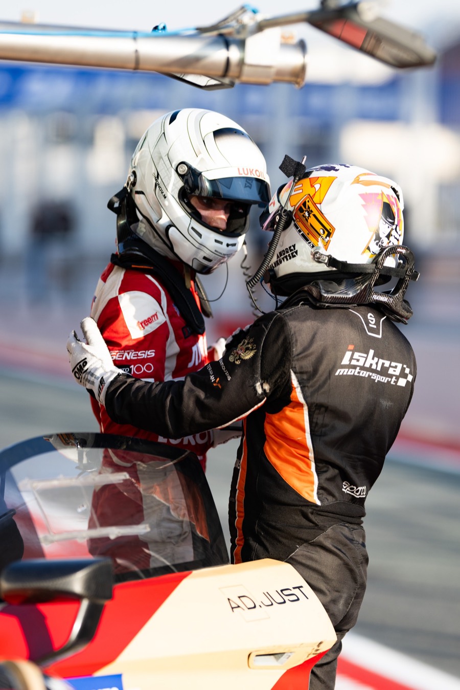 Two drivers in helmets embrace over the nose of the car after the finish