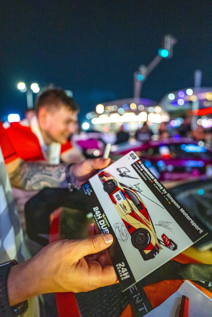 A just-signed card of the team's car held up over the barrier at night