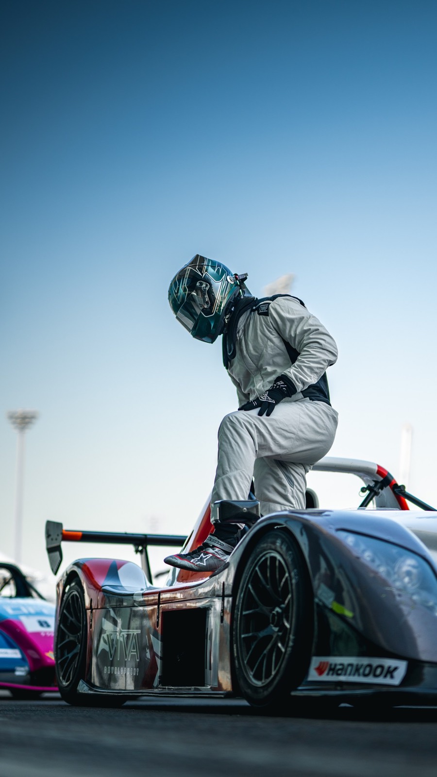 A driver climbing over the sill of the silver prototype under a clear sky, Yas Marina