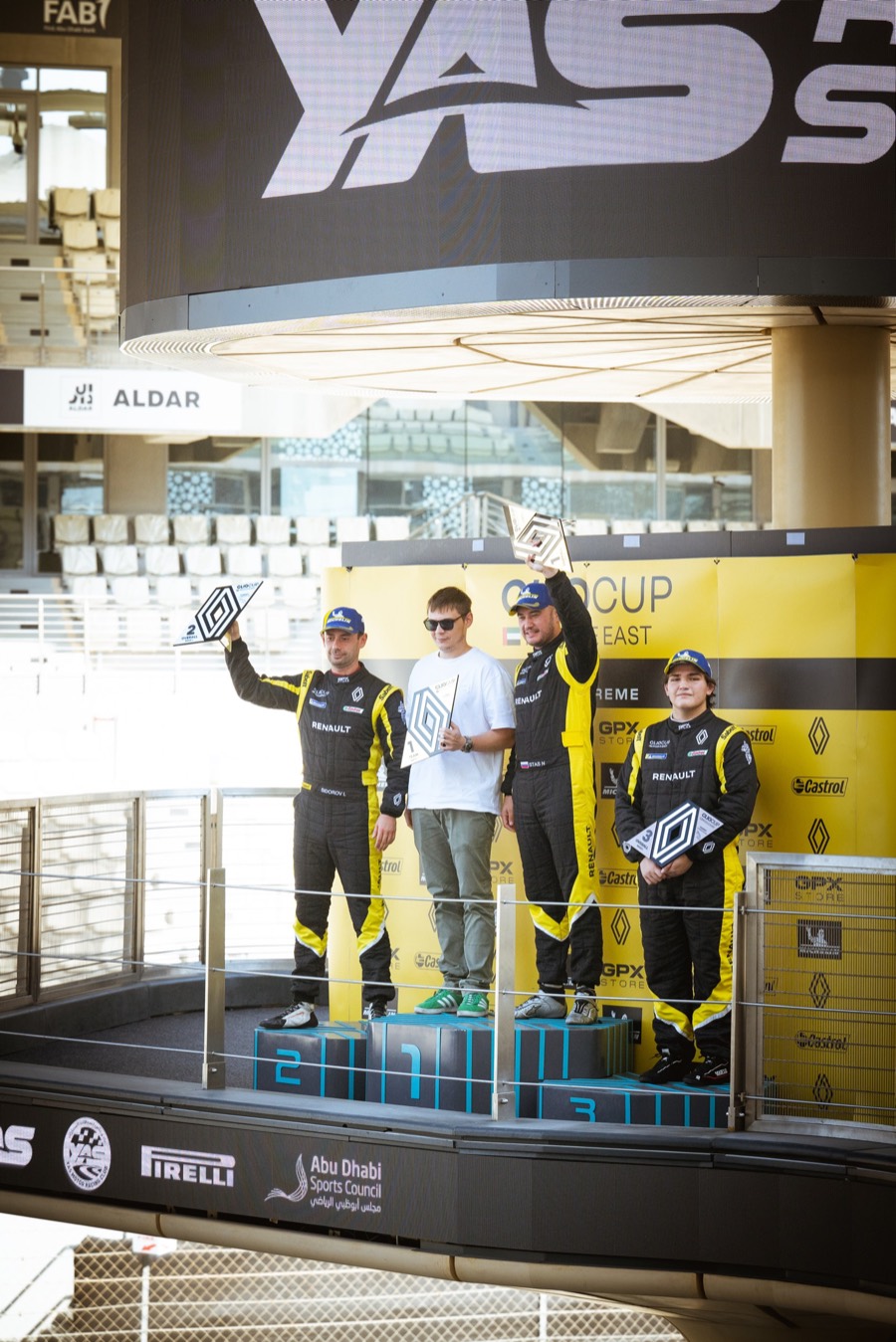 Three drivers with their trophies on the Clio Cup podium under the Yas Marina sign