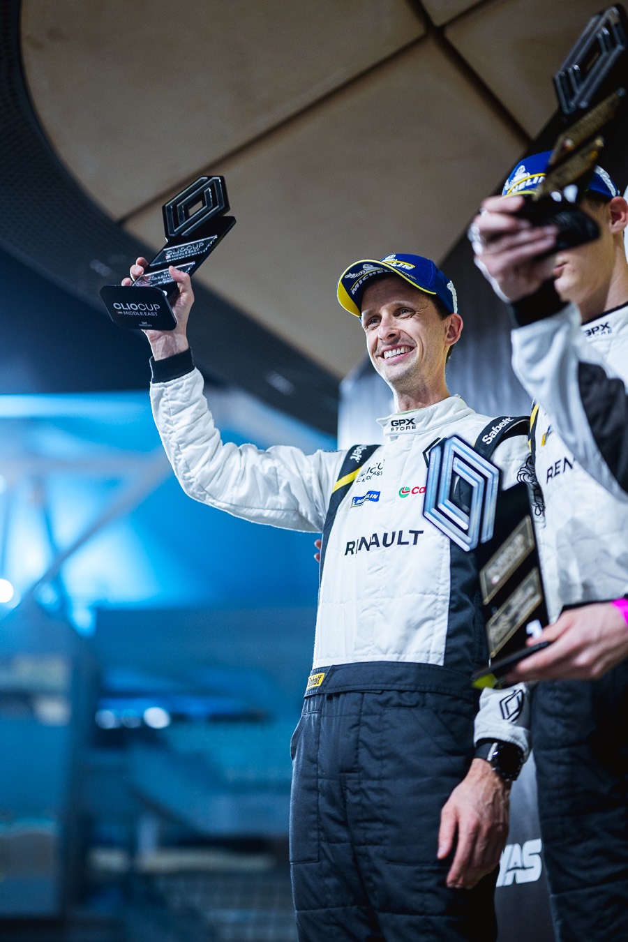 A driver lifting the Clio Cup trophy overhead, another alongside